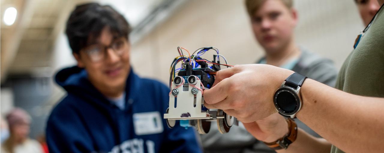 A small robot with a group of students standing around it